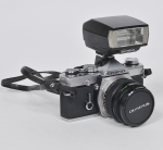COLECIONISMO - OLYMPUS - Câmera fotográfica analógica modelo OM-1 em metal e material sintético, lentes de 50mm com regulagem de foco. Estojo em couro com inscrição da manufatura. Med: 15 x 9 x 12cm