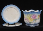 Lote composto por 03 peças em cerâmica esmaltada e vitrificada composto por um cachepot decorado com motivos florais e detalhes em baixo relevo (Med: 30 x 25cm) e duas travessas redondas rasas com faixas azuis. Med: 31cm