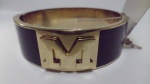 Bracelete em metal com a letra M ao centro.