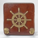 Suporte para chaves e bolsas em madeira de lei decorado com aplicações em latão no formato de leme de navio. Med. 23 x 23 cm.