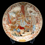 Medalhão em porcelana Satzuma Imperial com profusa decoração em representação de samurais em combate, envolvido por proeminente moldura em representação de predominância vegetal. Japão. Período Meiji. Circa de 1860. Pertenceu a Coleção de Armando Arruda Camargo. 38 cm.