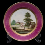 Prato em porcelana possivelmente francesa. Pasta dura. Borda com larga barra na cor bordeaux circundada por friso em ouro. Centro com paisagem, apresentando montanha, casas, árvore e personagens. França. Séc. XIX. 20,5 cm.
