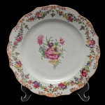 Prato com borda recortada, em porcelana Companhia das Índias, ornamentado em esmaltes da Famille Rose com guirlandas floridas centralizando composição floral. China. Dinastia Qing (1644-1917). Reinado Qianlong (1736-1785). 2ª Metade do séc. XVIII. 23,5 cm.