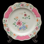 Prato em porcelana Companhia das Índias, ornamentado em esmaltes da Famille Rose. Borda recortada, ornamentada com arranjos florais alternados por reservas com treliças. Centro ornado com peônias e rochedo. China. Dinastia Qing (1644-1917). Final do séc. XVIII / início do séc. XIX. 22,5 cm.
