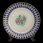Prato em porcelana Companhia das Índias, ornamentado em esmaltes da Famille Rose com realces a ouro. Borda ornada por losangos floridos sobre fundo azul cobalto, centralizando buquê com peônias. China. Dinastia Qing (1644-1911). Quianlong (1736-1795). 24 cm.