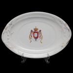 Travessa oval em porcelana inglesa com borda moldada em canelados, decorada nas laterais por flores realçadas a ouro. Centro ornamentado em policromia de esmaltes apresentando brasão de armas do Império português sob coroa. No verso, marca da manufatura Edward - Clarke  Longport  England, instalada e ativa nesta cidade de 1878 a 1880. 28 x 26 cm.