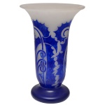 DEGUÉ  Vaso Art Déco em pasta de vidro acidado no formato de copo, lavrado em cameo e ornamentado por folhagens e volutas estilizadas em azul Royal sobre fundo leitoso. Bojo reto encimado por borda revirada. Pé circular largo e liso. Assinado Degué no bojo e marca gravada Made in France sob a base. Criação da manufatura Verrerie dArt Degué, fundada em Paris pelo mestre vidreiro e artista espagnol David Guéron e ativa de 1926 a 1939. 39 x 25 cm.