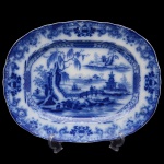 Travessa de louça inglesa de formato retangular e bordas onduladas, conhecida como borrão. Apresenta decoração em esmalte de tom azul cobalto sobre fundo branco. Ao centro cena lacustre em reserva com pagode ao fundo. Inglaterra. Final do séc. XIX.  44 x 35 cm.