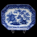 Travessa de louça inglesa de formato retangular e cantos chanfrados conhecida como borrão. Apresenta decoração em esmalte de tom azul cobalto sobre fundo branco. Ao centro cena lacustre com arvores, casario. Inglaterra. Final do séc. XIX.  39 x 30 cm.