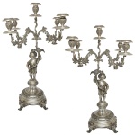 Par de candelabros para cinco velas em prata portuguesa repuxada e cinzelada. Hastes ornamentadas por figuras de meninos segurando flores, de pé sobre pedestais, encimadas por braços recurvos ornados por folhagens e centralizando ponteiras altas com castiçais. Bases circulares abobadadas com frisos florais, apoiadas em pés recurvos. Contraste da cidade do Porto, Javali, datavel de circa de 1920/25. Marcas de prateiro. 61 cm. Peso aprox. 5K 520 gramas. Peça adquirida do acervo do Antiquário Theo d' Aprile.
