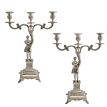 Raro par de candelabros para três velas em prata portuguesa ou luso-brasileira repuxada e cinzelada. Hastes ornamentadas por figuras romanas sobre pedestais, segurando tochas encimadas por pares de braços recurvos centralizando ponteiras com castiçais. Bases quadrangulares e almofadadas, ornadas por frisos florais e apoiadas em pés de garra. Contrastes da cidade do Porto, P Coroa, marcas de prateiro atribuíveis a Luís António Rodrigues de Araújo e punções do ensaiador da Bahia, Manuel Eustáquio de Figueiredo, que também trabalhou em Guimarães e remarcou peças na cidade do Porto. Moitinho P-428 p.266 e BR-7 p.344. 41 (altura) x 33 cm. 3k596 gramas.