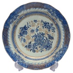 Prato em porcelana Companhia das Índias, com borda recortada, decorado em azul cobalto e adornos a ouro com bordas florais e frisos estilizados. Centro ornamentado por composição com peônias e folhagens. China. Reinado Qianlong (1736-1795). No verso, etiqueta da coleção Ari Bragança e Bourbon No 406. 35 cm.
