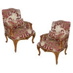 Par de poltronas em madeira esculpida e dourada, estilo Louis XV, ornadas com frisos canelados e adornos florais. Encostos retos e arqueados com braços apoiados em montantes recurvos. Assentos abaulados com saias onduladas centralizando composições realçadas por concheados. Pernas curvilíneas e pés sobre pequenas sapatas. Estofamento em tecido com larga estampa floral sobre fundo de cor rubi. 107 x 77 x 64 cm.