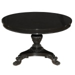 Mesa de apresentação em madeira escura lustrada, com tampo circular liso apoiado em saia reta com borda inferior saliente. Coluna central, profusamente esculpida e ornada com gomos e frisos perolados, assentada em base triangular lisa e recortada com pernas rematadas por volutas e pés de garra. 74 x 110 cm.