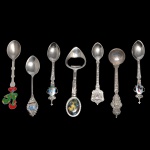 Conjunto de 7 colheres de metal prateado com decoração e materiais variados. 12.5 cm (maior). 10.5 cm (menor).