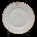 Prato raso de porcelana Vista Alegre, pertencente ao Serviço do Hotel Copacabana Palace, Rio de Janeiro. Superfície de fundo branco com borda dourada. Iniciais entrelaçadas a ouro. No fundo marca da manufatura, Vista Alegre, Portugal. 25 cm.