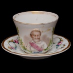 VIEUX PARIS  Xícara e pires em porcelana francesa, ornamentados em esmaltes policromados e frisos a ouro. Bojo de formato levemente revirado apresentando busto do rei Henri IV da França. Alça lateral em asa. Prato com borda moldada em gomos, decorado por dupla guirlanda florida e rosas. Séc. XIX. 9 x 13 cm. 17 cm (pires).