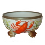 WMF - Saladeira alemã em porcelana decorada em policromia com folhagens. Bowl circular fundo, apoiado em pés moldados no formato de lagostas esparramadas sobre o bojo. Borda em metal prateado liso. Numerada no fundo e marcada no metal. 12 x 21 cm.