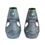 Par de vasos de formato Double gourd em metal, ornados em esmalte prateado, decorados com estilizações. Frisos, bordas e alças laterais vazadas, esmaltados em tons verdes e realçados por cabochões em pedras coloridas. Faltam 3 pequenas pedras. 19 x 9 cm. Este lote encontra-se em Belo Horizonte, MG, e só estará disponível em nossa loja a partir do dia 13 de Outubro.