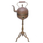 Chaleira com seu braseiro, provavelmente do Oriente Médio ou do Marrocos, em cobre lavrado e martelado com estilizações, arcos e arabescos. Bojo globular com alça superior e bico recurvo. Tampa rematada por pega em pião. Base com coluna torneada e anelada apoiada em pernas recurvas. 104 x 41 cm. Este lote encontra-se em Belo Horizonte, MG, e só estará disponível em nossa loja a partir do dia 13 de Outubro.