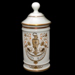 Pote de farmácia em porcelana francesa de formato cilíndrico, com tampa cônica rematada por bolota. Bojo moldado com frisos anelados e filetes dourados, ornamentado em policromia com vaso e serpente ladeado por folhagens. Traz a inscrição Pulvis Alginat. Sob a base, marcas da manufatura de Limoges Au Pot de Gallien e Produits Dentaires Biodica. Séc. XX. 27 cm.
