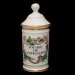 Pote de farmácia em porcelana francesa de formato cilíndrico, com tampa cônica rematada por bolota. Bojo moldado com frisos anelados e filetes dourados, ornamentado em policromia com folhagens e flores.  Traz a inscrição Poudre de Cantharide. Sob a base, marcas da manufatura de Limoges, France Au Pot de Gallien. Séc. XX. 28 cm.
