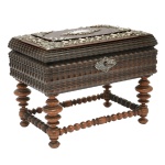 Caixa de música porta joias com base, de formato retangular em madeira nobre com adornos provavelmente em prata. Bordas esculpidas e ornadas por tremidos superpostos. Frente com fechadura, espelho e chave. Tampo ornamentado por friso floral repuxado e cinzelado, encimado por painel com cantoneiras e reserva central lavradas. Interior forrado em veludo vermelho, com espelho e divisórias centralizando pequena figura de bailarina acionada por movimento a corda. Base construída com colunas retas e aneladas, reunidas à base por traves de mesmo desenho e rematadas por pés de bolacha. 19 x 24 x 16 cm. Funcionando. Apresenta desgaste no tecido.