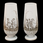 Par de floreiras de formato alongado, em opalina leitosa, ornamentadas em sépia por cenas de pescaria com crianças e anjos. Bojos no formato de copos, apoiados em bases circulares lisas e ornadas por filetes azuis e frisos dourados. 25.5 cm.