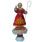 Menino Deus - Imagem esculpida em madeira representando o Menino Deus, nu, sob camisola e vestido tecido com fios dourados. A cabelos são dourados e traz um discreto sorriso. Séc. XIX. 16.5 cm (imagem). 42 cm (medida completa). A imagem foi restaurada recentemente e colocada sobre uma nova peanha.