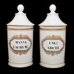 Par de potes de farmácia de porcelana francesa. Superfície branca apresentando rótulo com as inscrições: MANNA CACRYM e UNG ARCAEL, envolto em moldura octogonal em esmaltes azul e dourado. França. Séc. XIX. 26 cm.