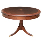 Mesa inglesa para jogo em madeira nobre ornamentada em parqueterie. Tampo circular com borda clara e rosácea embutida ao centro. Saia lavrada com painéis emoldurados alternados por gavetas almofadadas. Coluna central lisa e anelada, sustentada por pernas recurvas, filetadas e rematadas por pés de garra em bronze dourado. 77 x 109 cm. Lote pertencente ao acervo de tradicional família paulistana de Américo Moreira dos Santos e Anella Mafalda Malzoni. Este lote encontra-se na residência em SP e a retirada devera ser feita a partir do endereço com a orientação da organizadora do leilão.