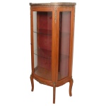 Vitrine estilo francês Louis XV em madeira nobre, de formato retangular, ornamentada por galeria, frisos e adornos em bronze ormolu. Porta e laterais envidraçadas, suavemente abauladas, ladeadas por montantes lisos. Interior com prateleiras em vidro sobre fundo em tecido de cor vinho. Saia inferior recortada e apoiada em pés recurvos. Séc. XX. 138 x 68 x 30 cm. Lote pertencente ao acervo de tradicional família paulistana de Américo Moreira dos Santos e Anella Mafalda Malzoni. Este lote encontra-se na residência em SP e a retirada devera ser feita a partir do endereço com a orientação da organizadora do leilão.
