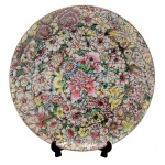 Prato raso de forma circular de porcelana chinesa. Decoração com detalhes em ouro e flores de vários tipos e cores formando no centro grande peônias. Apresenta selo da Casa Castro  São Paulo. 24 cm. Lote pertencente ao acervo de tradicional família paulistana de Américo Moreira dos Santos e Anella Mafalda Malzoni.