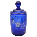 Pote para algodão em vidro na cor azul cobalto. Formato cilíndrico com decoração de flores brancas. Tampa com frisos dourados e pega na forma de esfera. 20 x 9 cm. Lote pertencente ao acervo de tradicional família paulistana de Américo Moreira dos Santos e Anella Mafalda Malzoni.