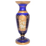 Floreira de vidro de cor Bleu du Roi, ricamente ornamentada em policromia por arranjos florais sobre fundo dourado distribuídos em painéis lobulados. Bordas lisas. 37 x 13 cm. Lote pertencente ao acervo de tradicional família paulistana de Américo Moreira dos Santos e Anella Mafalda Malzoni.