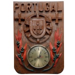 Relógio de parede montado em placa de madeira de formato retangular com quinas inferiores recortadas. Apresenta mostrador circular ladeado por galhos lavrados em alto relevo. Parte superior esculpida com brasão do Império português e cruzes da Ordem de Cristo sob o nome de Portugal. 60 x 42 cm. Lote pertencente ao acervo de tradicional família paulistana de Américo Moreira dos Santos e Anella Mafalda Malzoni.