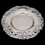 Salva funda prata portuguesa repuxada e cinzelada. Borda larga, ornamentada por volutas, ramos floridos, drapeados, folhagens e treliças vazadas. Fundo gravado com adornos florais. Contraste do Porto Javali 2º Título e marca de prateiro. 21 cm. 177 gramas. Lote pertencente ao acervo de tradicional família paulistana de Américo Moreira dos Santos e Anella Mafalda Malzoni.