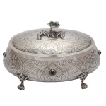 Bonbonnière em prata brasileira repuxada e cinzelada, de formato ovalado, ornamentada por volutas, folhagens e florões. Bojo abaulado ornado com pequenos cabochões em pedra verde. Tampa abobadada com pega no formato de flor. Pés recurvos rematados por garras. Contraste da prata brasileira 833 mls e marca de prateiro ilegível. 11 x 18 x 12 cm. 440 gramas. Lote pertencente ao acervo de tradicional família paulistana de Américo Moreira dos Santos e Anella Mafalda Malzoni.
