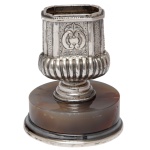 Porta canetas em prata brasileira repuxada e cinzelada. Bojo circular moldado com gomos até meia altura, encimado por recipiente quadrangular ornamentado por faixas verticais centralizando reservas com florões. Base cônica, assentada em peanha circular em ágata de cor marrom, apoiada sobre duas bordas lisas. Marca de Silver Brazil. 10 x 8 cm. 363 gramas. Lote pertencente ao acervo de tradicional família paulistana de Américo Moreira dos Santos e Anella Mafalda Malzoni.