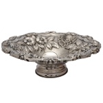 Fruteira circular baixa em prata brasileira repuxada e cinzelada, ornada por borda recortada em volutas e ornamentada por flores e folhagens em alto relevo. Base construída em anelados lisos e superpostos. Não apresenta contrastes. 10 x 31 cm. 445 gramas. Lote pertencente ao acervo de tradicional família paulistana de Américo Moreira dos Santos e Anella Mafalda Malzoni.