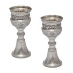 Par de pequenos castiçais de metal prateado. Bases na forma de cone invertidos. 12 cm. 1 com amassado.  Lote pertencente ao acervo de tradicional família paulistana de Américo Moreira dos Santos e Anella Mafalda Malzoni.