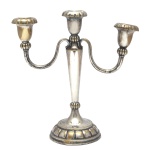 Candelabro para três velas de metal prateado. Coluna sustentando dois braços com bobeche e uma central. Base circular com godrões. No estado. 25 x 24 cm.  Lote pertencente ao acervo de tradicional família paulistana de Américo Moreira dos Santos e Anella Mafalda Malzoni.