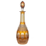 BACCARAT - Licoreiro em cristal doublê, amarelo e translúcido, de forma alongada, com elaborada lapidação manual geométrica. Listra central amarela com sequência de formas elípticas translúcidas, ladeada por lapidação obliqua, bico de jaca. Gargalo canelado e tampa alongada, com a mesma decoração do bojo. França. Séc. XX. 30 cm.