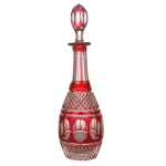 BACCARAT - Licoreiro em cristal doublê, vermelho e translúcido, de forma alongada, com elaborada lapidação manual geométrica: lista central vermelha com sequência de formas elípticas translúcidas, ladeada por lapidação obliqua bico de jaca. Gargalo canelado e tampa alongada, com a mesma decoração do bojo. França. Séc. XX. 30 cm.