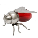 Original pote italiano para mel no formato de abelha com abdômen em vidro vermelho e montagem em metal prateado. Tampa com dobradiça, no formato das asas e apoio sobre três pares de pernas. Sob a base, numeração 176 com iniciais I.F.S. do artista e designer Israel Freeman & Son, de Milão. Início do séc. XX. 9 x 16 cm. Este lote encontra-se em Belo Horizonte, MG, e só estará disponível em nossa loja a partir do dia 13 de Outubro.