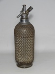 DIVERSOS, uma (1) antiga garrafa sifonada, confeccionada em vidro moldado, incolor e translúcido, monture em malha metálica, Made in England, sinais de usos e oxidação, medindo 34 cm altura.
