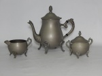 METAL PRATEADO, três (3) peças: 1 bule; 1 açucareiro e 1 cremeira, todos lisos e bojudos com extremidades relevadas em elementos vegetalistas, volutas e canelados, todas sem marca de manufatura aparente, medindo a maior peça 22 cm altura.