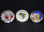 PORCELANA, três (3) pratos decorativos policromados: 1 souvenir de São Luís, MA  Ladeira do Comércio, medindo 18,5 cm diâmetro; 1 com o mapa do brasil, medindo 20 cm diâmetro; 1 com diversos pontos turísticos do rio de janeiro, borda com friso dourado, medindo 20,5 cm diâmetro.