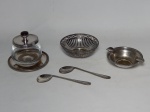 METAL PRATEADO E VIDRO, cinco (5) itens: 1 cinzeiro circular, marcado Sheffield Plate, medindo 10 cm diâmetro; 1 pequena cesta com treliça vazada, medindo 10 cm diâmetro; 2 colheres para alimentação de criança, manufatura BELLINI, apresenta desgastes; 1 porta geleia, incolor e translucida com tampa e presentoir em metal prateado, sem marca de manufatura aparente, apresenta desgastes.