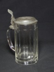 VIDRO ALEMÃO, um (1) antigo tankard do primeiro quartel do século XX, período Primeira Grande Guerra, incolor e translúcido com caneluras verticais, capacidade 1/2 litro, marcada na base em relevo na própria modelagem com as letras SG dentro de uma coroa (Stein Germany, fabricante Saxão, marca usada desde o último quartel do século XIX), tampa em pewter relevada com a cruz de ferro e o ano 1914 encimado por coroa e guirlanda de folhas de café em torno, medindo 19,5 cm altura, sinais de uso.